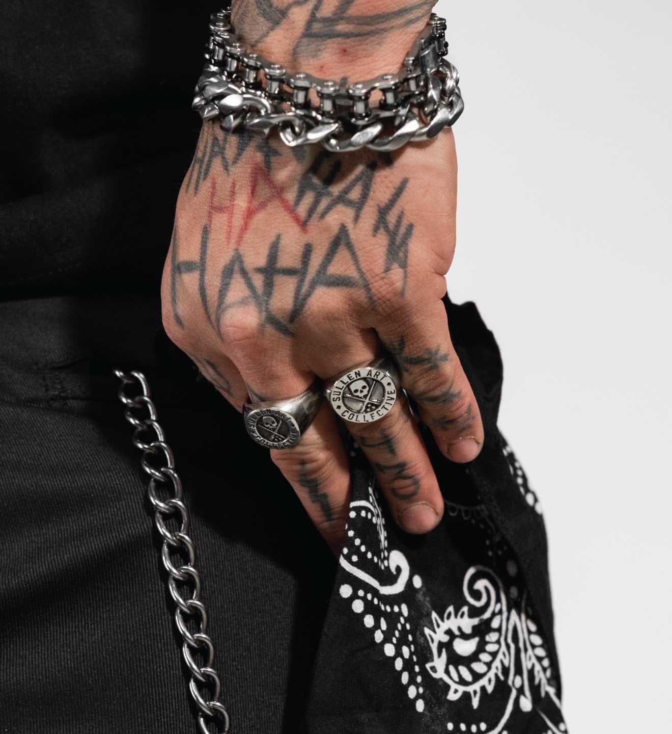 Hand with tattoos wearing multiple bracelets and rings on a plain background