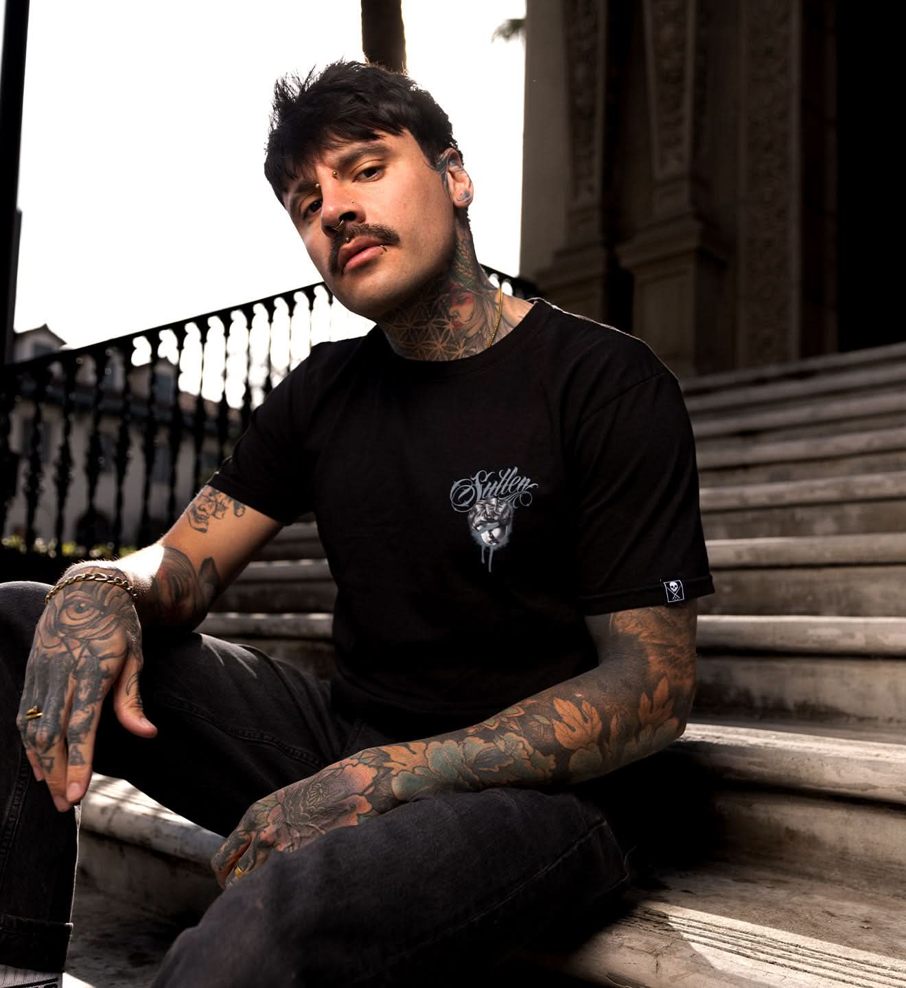Man with tattoos wearing a black t-shirt sitting on steps outdoors