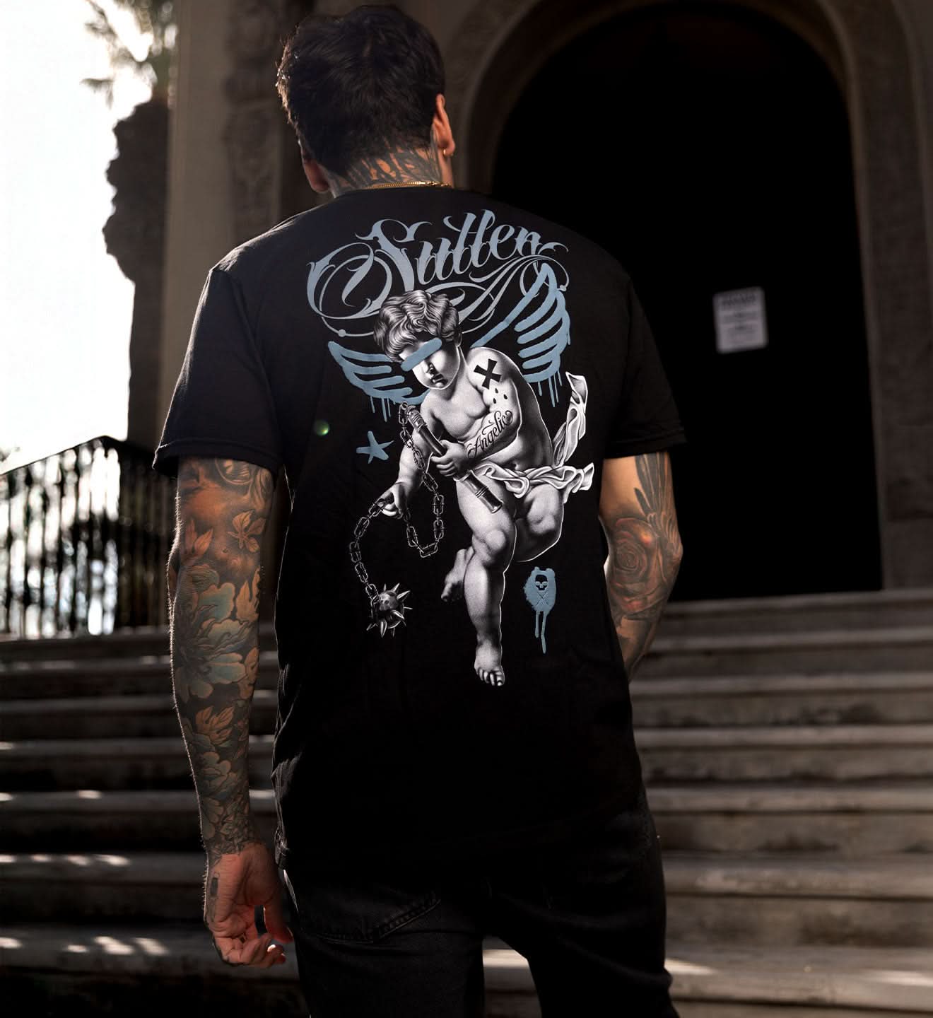 Person wearing a black t-shirt with a graphic design on the back, standing outdoors.