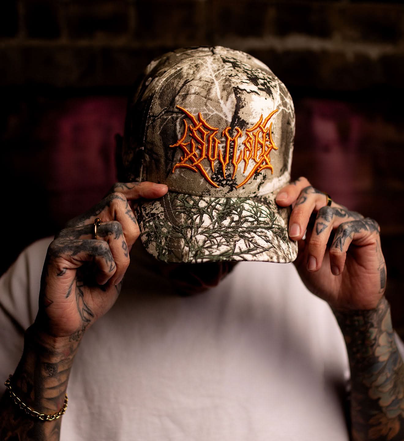 Person holding a camouflage cap with a logo against a blurred background