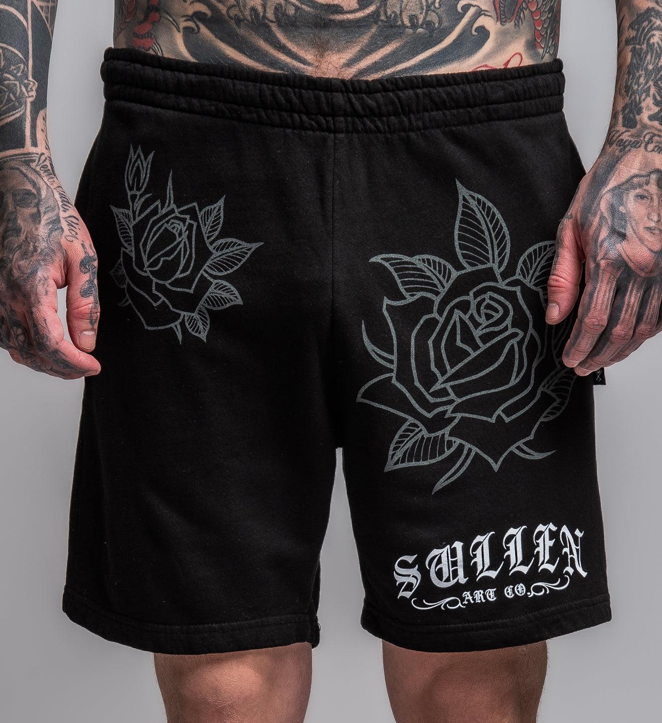 Black shorts with rose designs and 'Sullen Art Co.' branding on a gray background