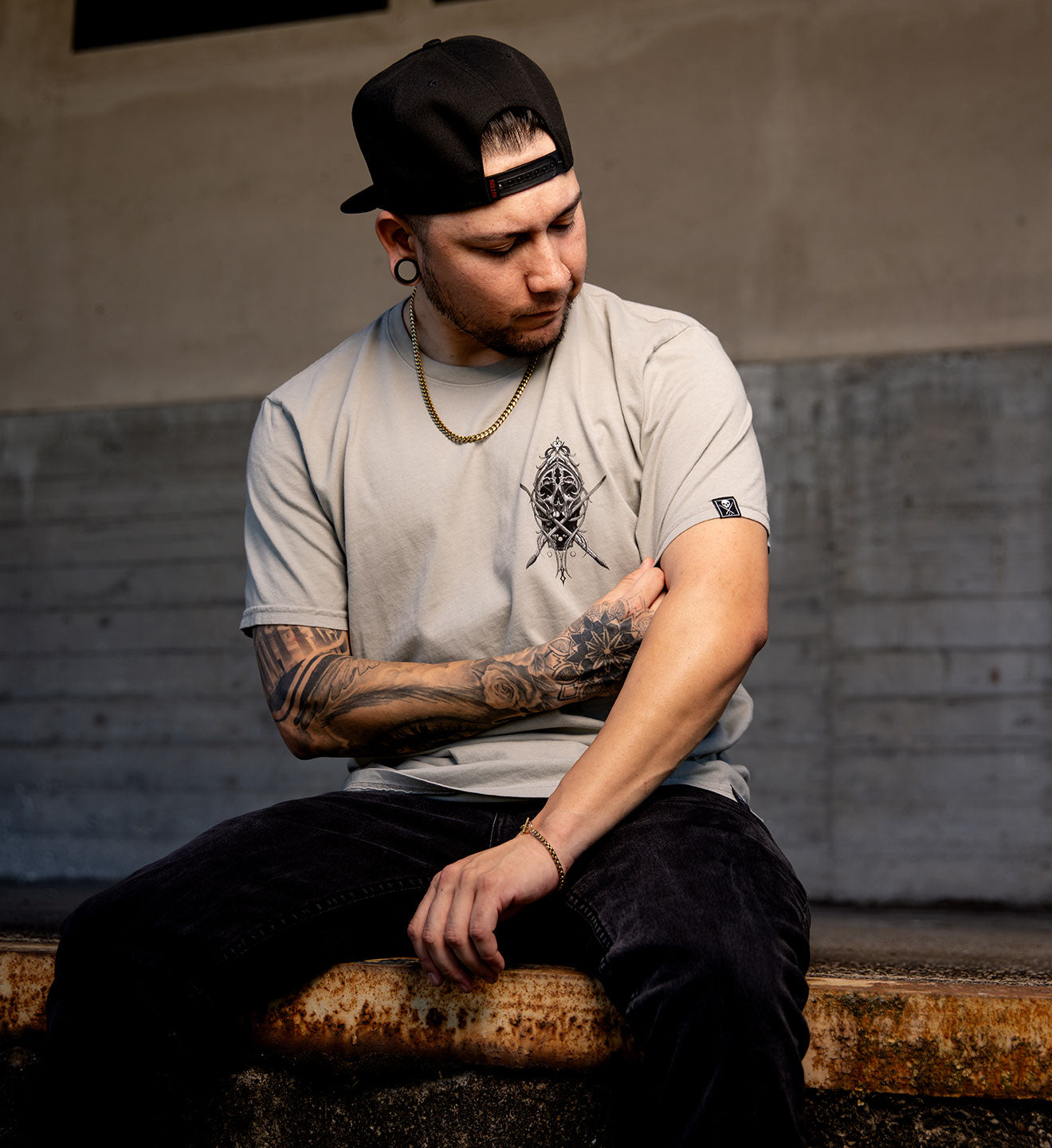 Man sitting on a bench wearing a cap and casual clothing with tattoos visible.