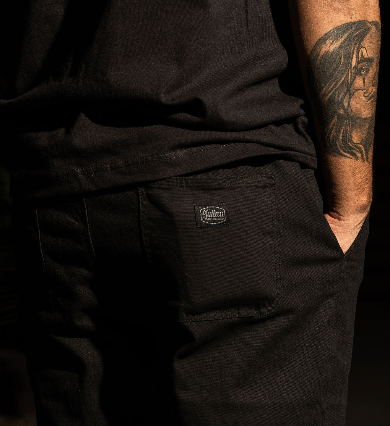 Person wearing black pants with a visible brand logo on a dark background