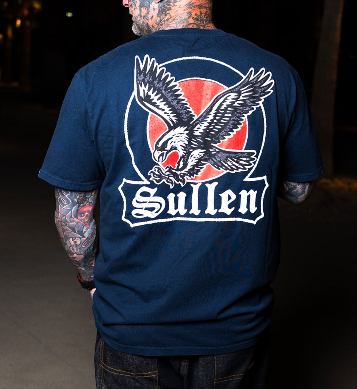 Person wearing a navy blue t-shirt with a logo and the word 'Sullen' on the back.