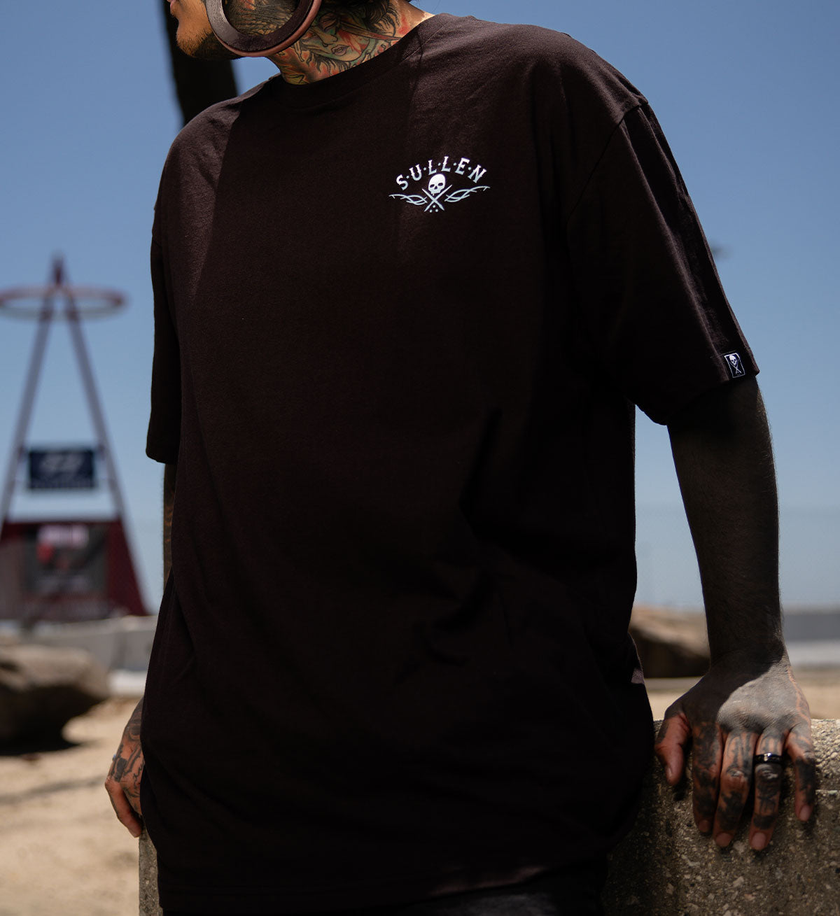 Person wearing a black t-shirt with a logo, standing outdoors with a clear blue sky.
