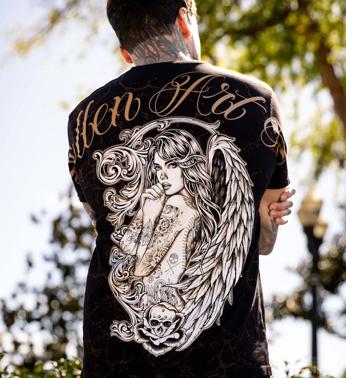 Person wearing a black t-shirt with a large angel design and text on the back, standing outdoors.
