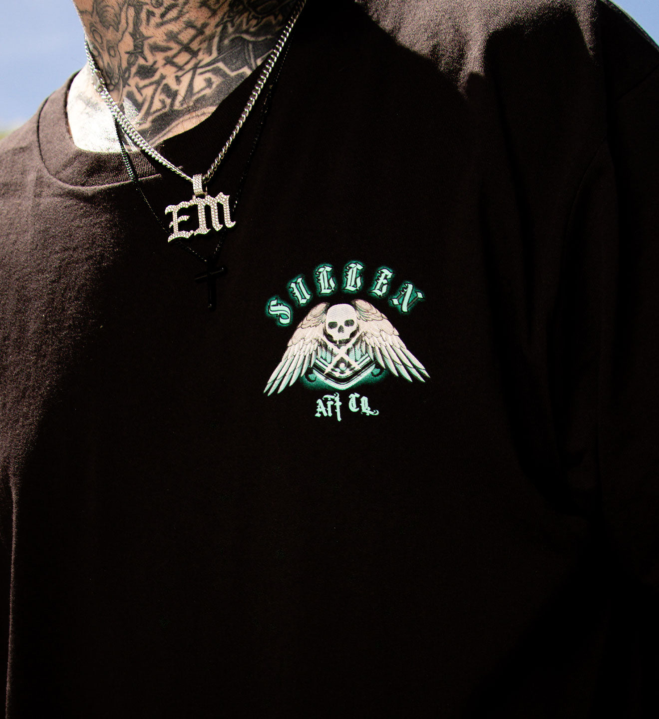 Black hoodie with embroidered logo and 'EM' necklace on a plain background