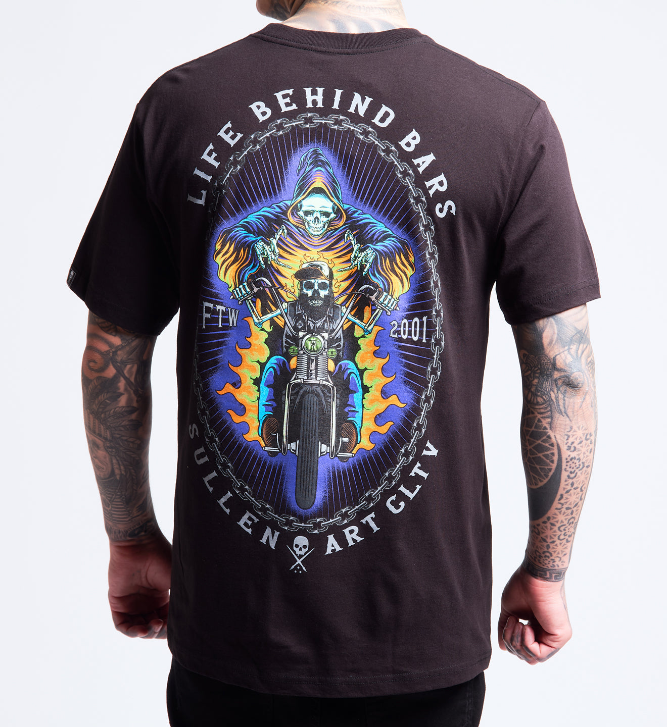 Person wearing a black t-shirt with a graphic design of a skeleton on a motorcycle and text 'Life Behind Bars' on the back.