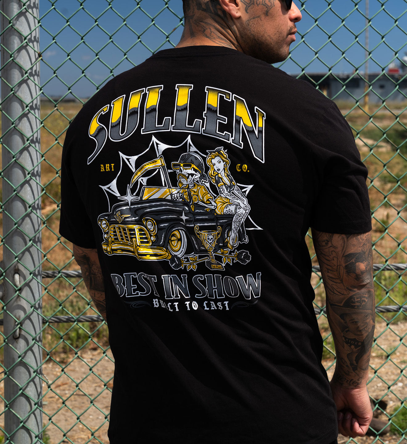 Person wearing a black t-shirt with 'Sullen' graphic design in an outdoor setting.