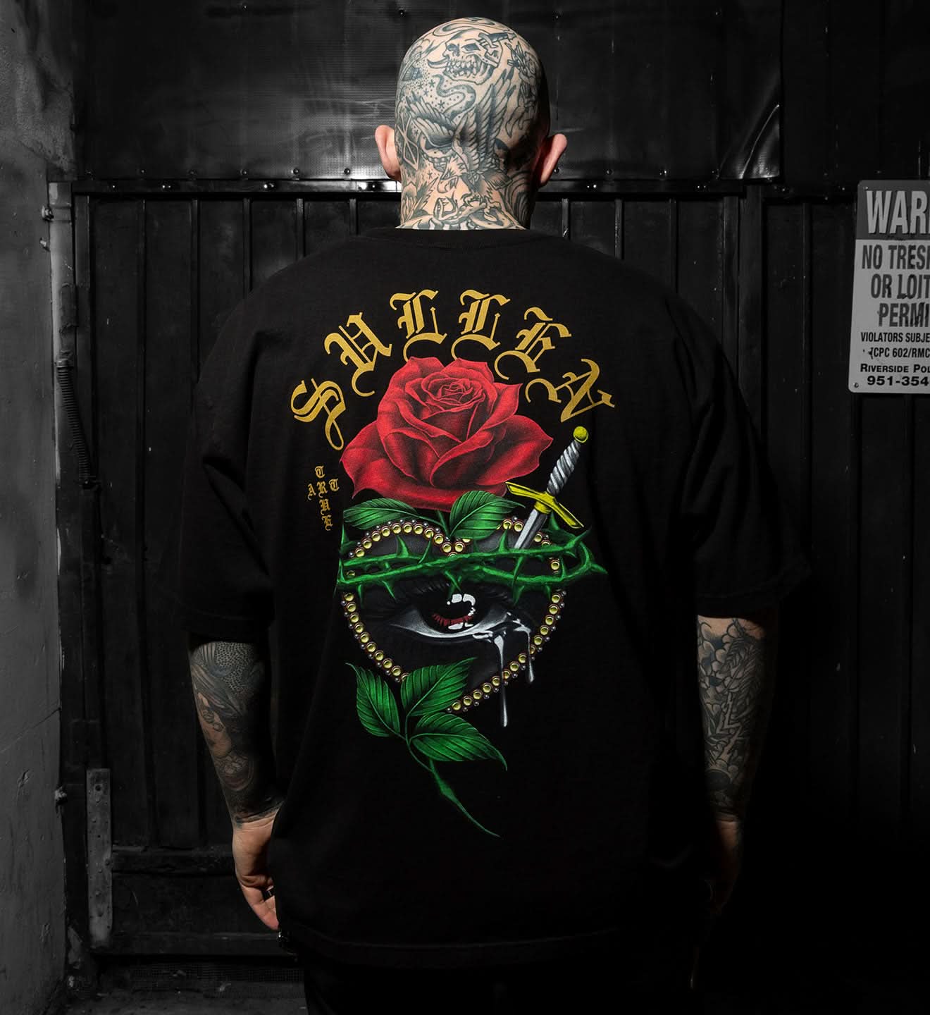 Person wearing a black t-shirt with a colorful graphic design on the back, featuring a rose and text.