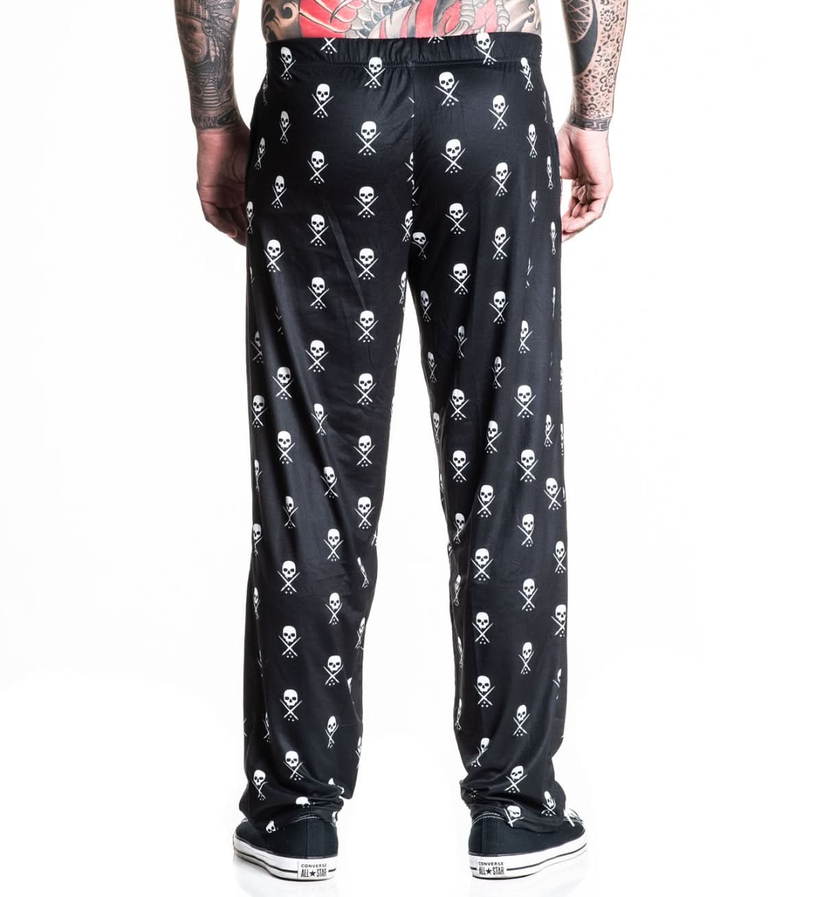 Black pants with skull and crossbones pattern worn by a person on a white background
