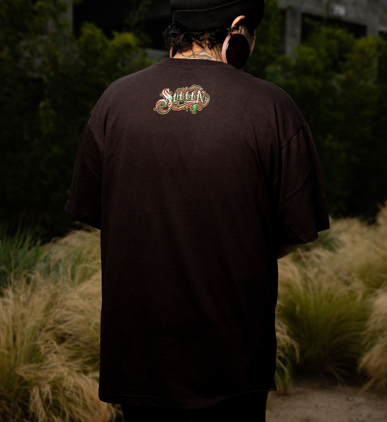 Person wearing a black t-shirt with a logo on the back, standing outdoors.