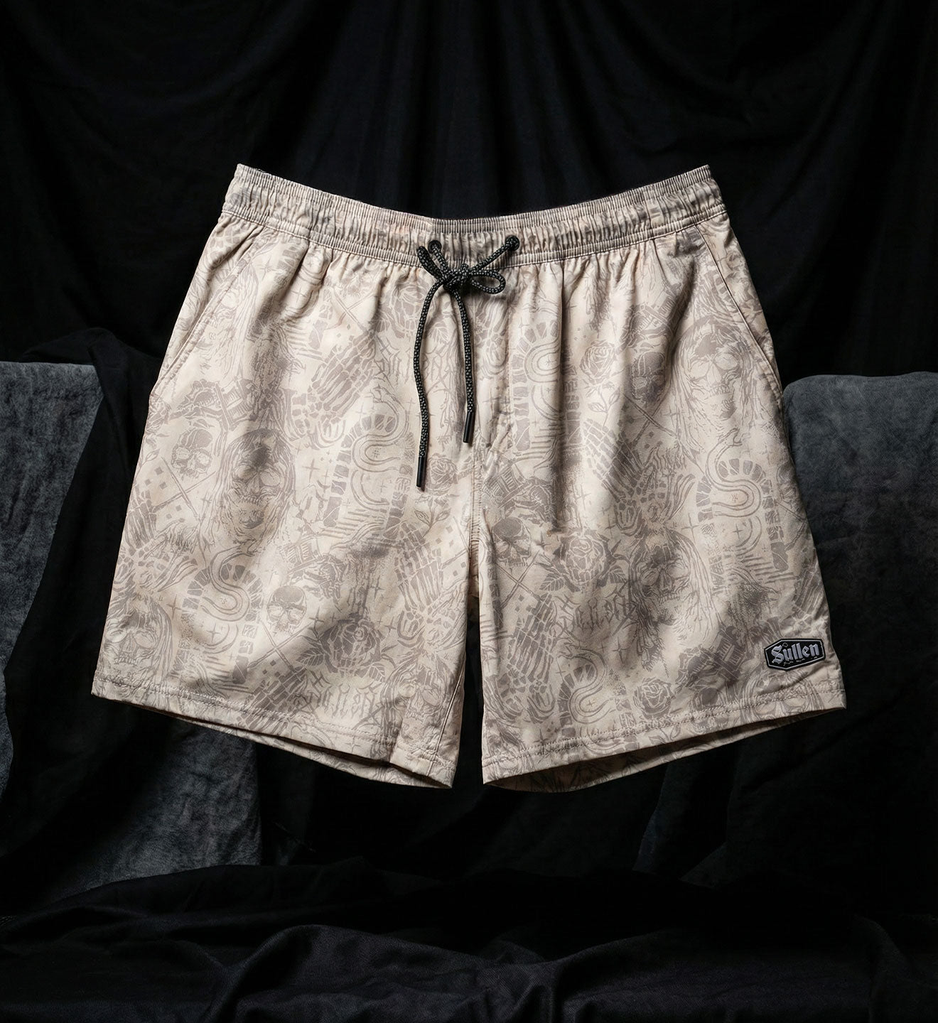 Beige patterned shorts with a brand logo on a black background