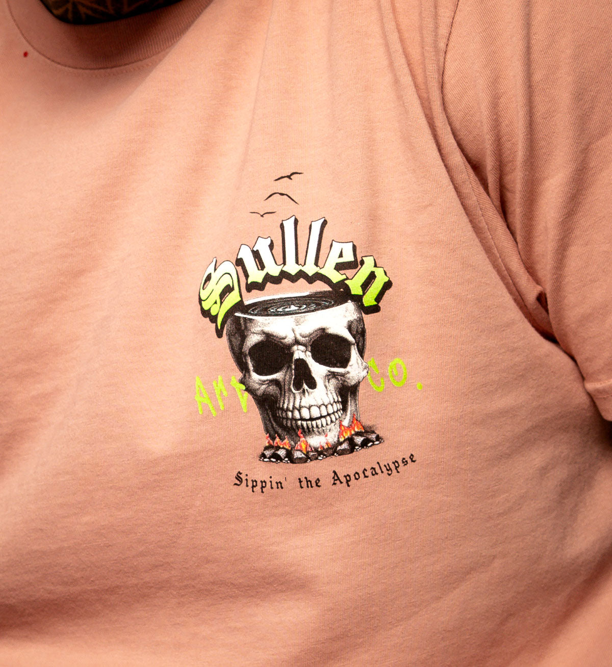 Pink t-shirt with a skull graphic and text on a plain background