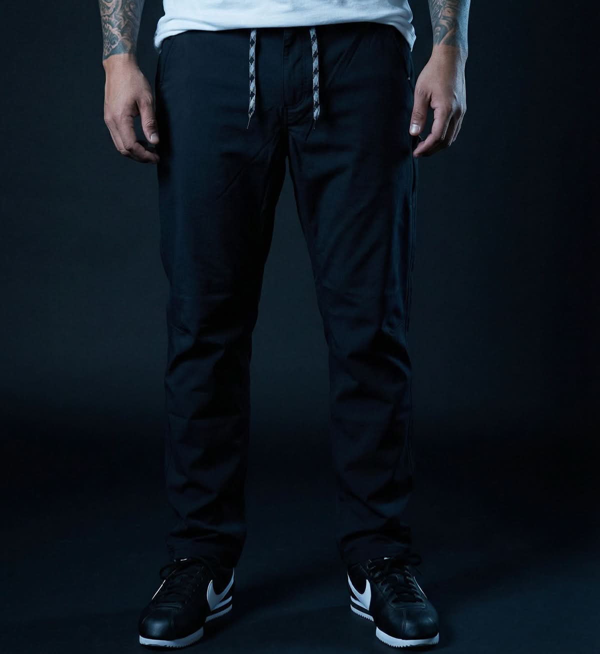Person wearing black pants and black sneakers on a dark background