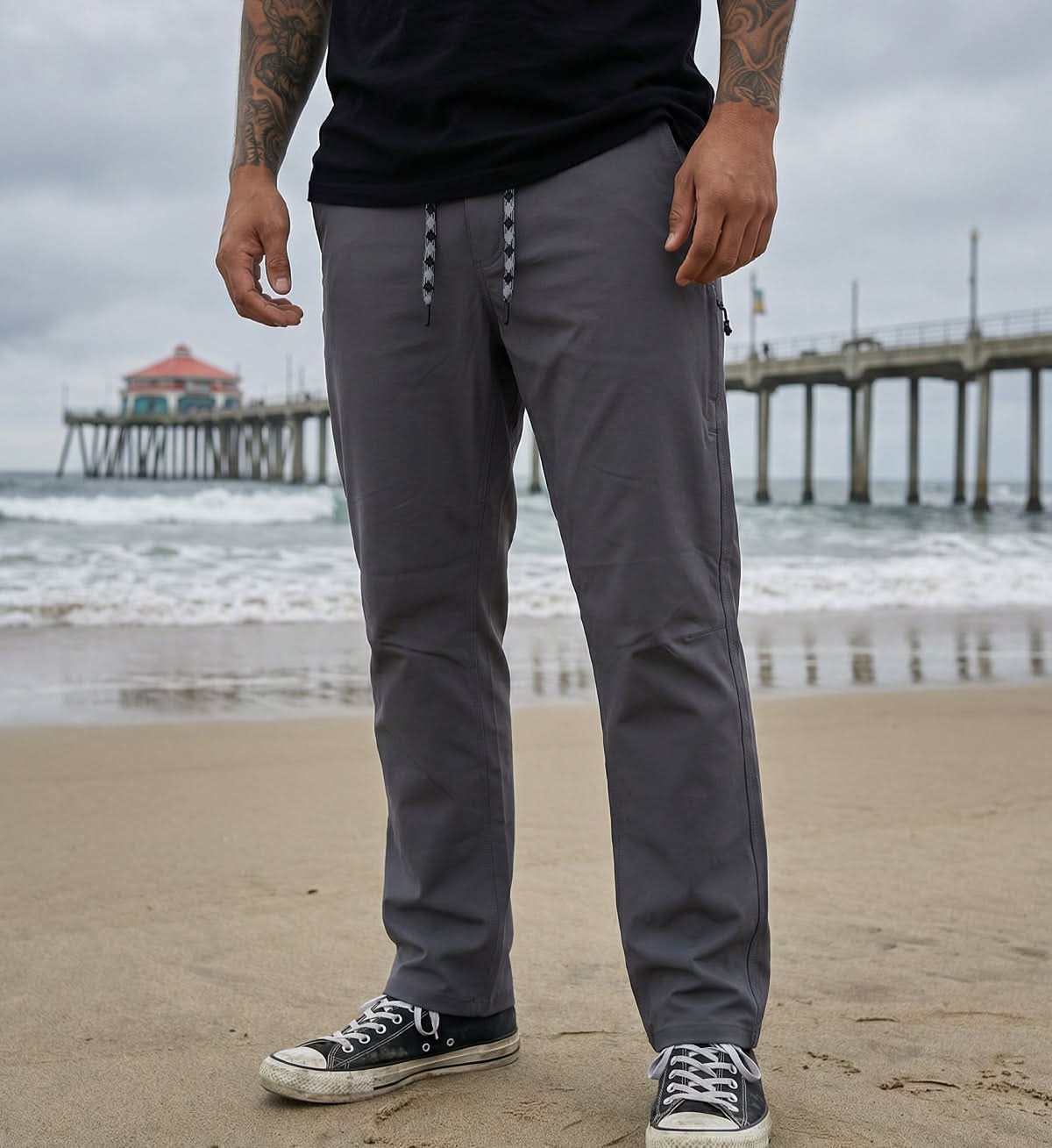 Person wearing gray pants standing on a beach with a pier in the background