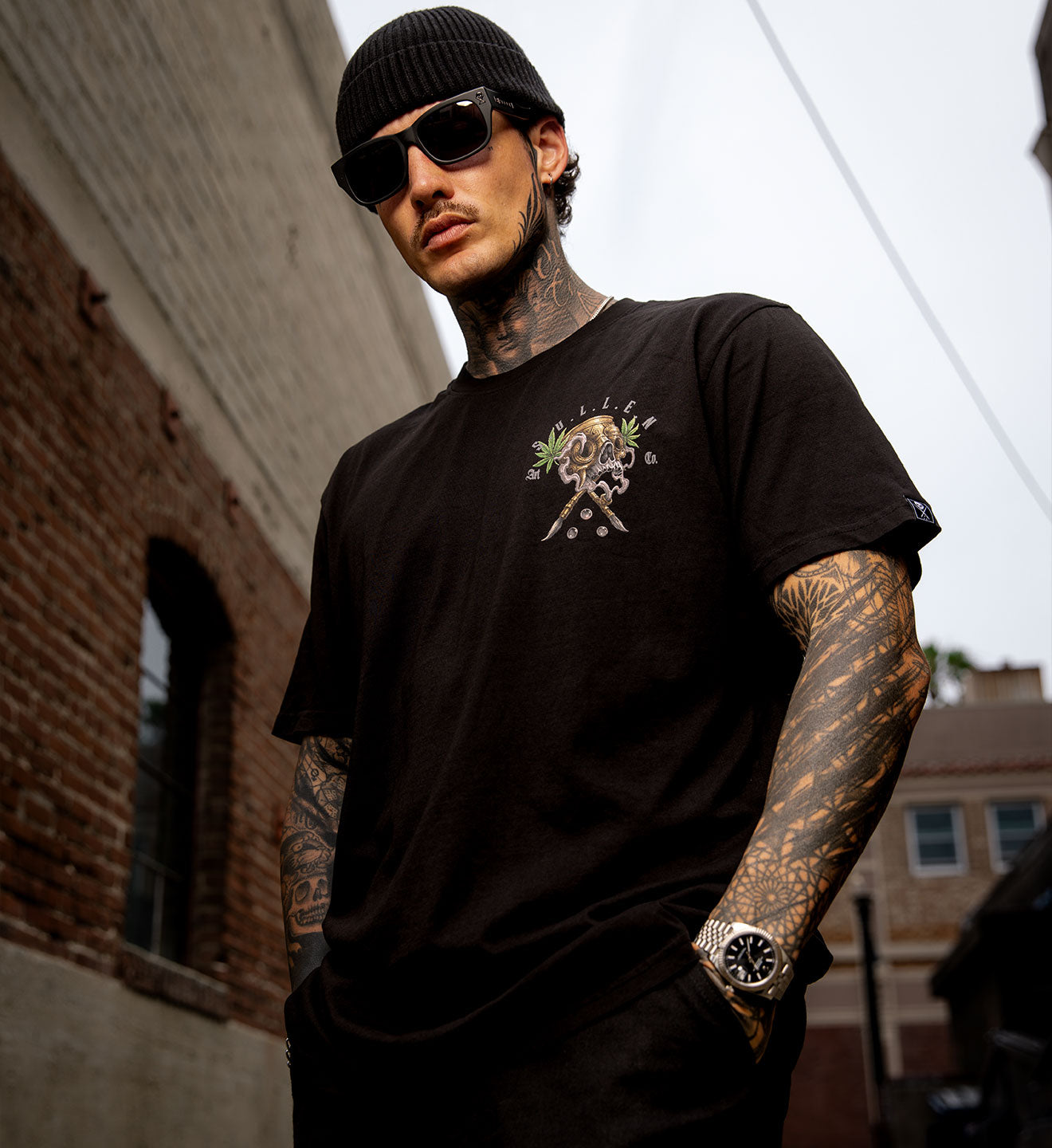 Man wearing a black t-shirt with a graphic design, sunglasses, and a beanie outdoors.