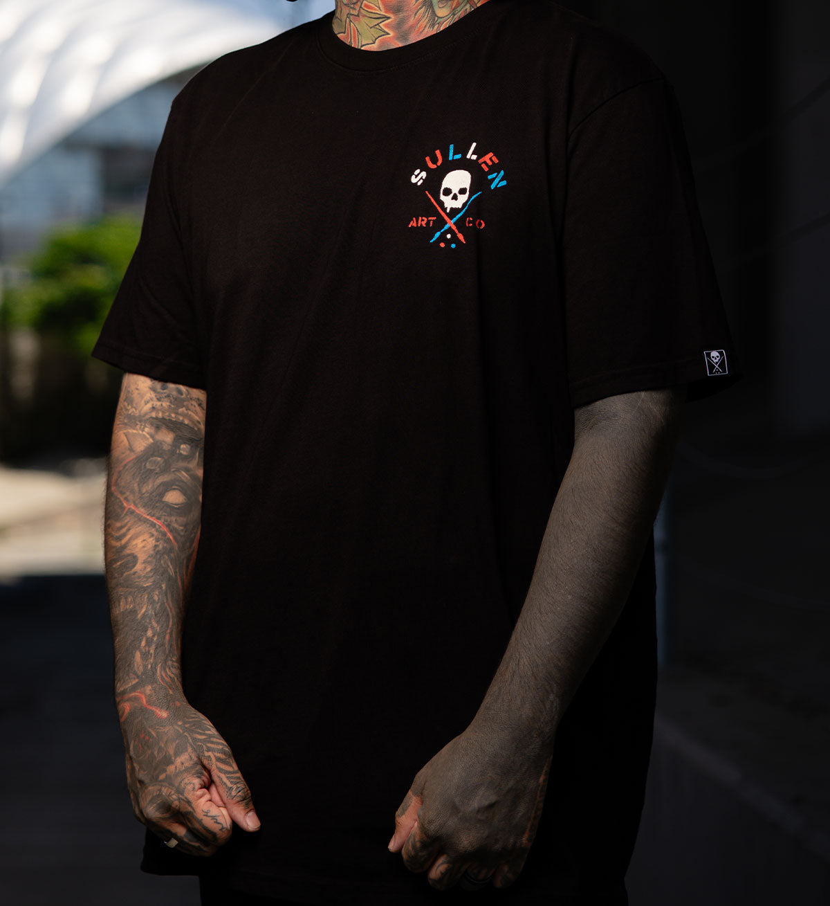 Person wearing a black t-shirt with a logo, standing outdoors.