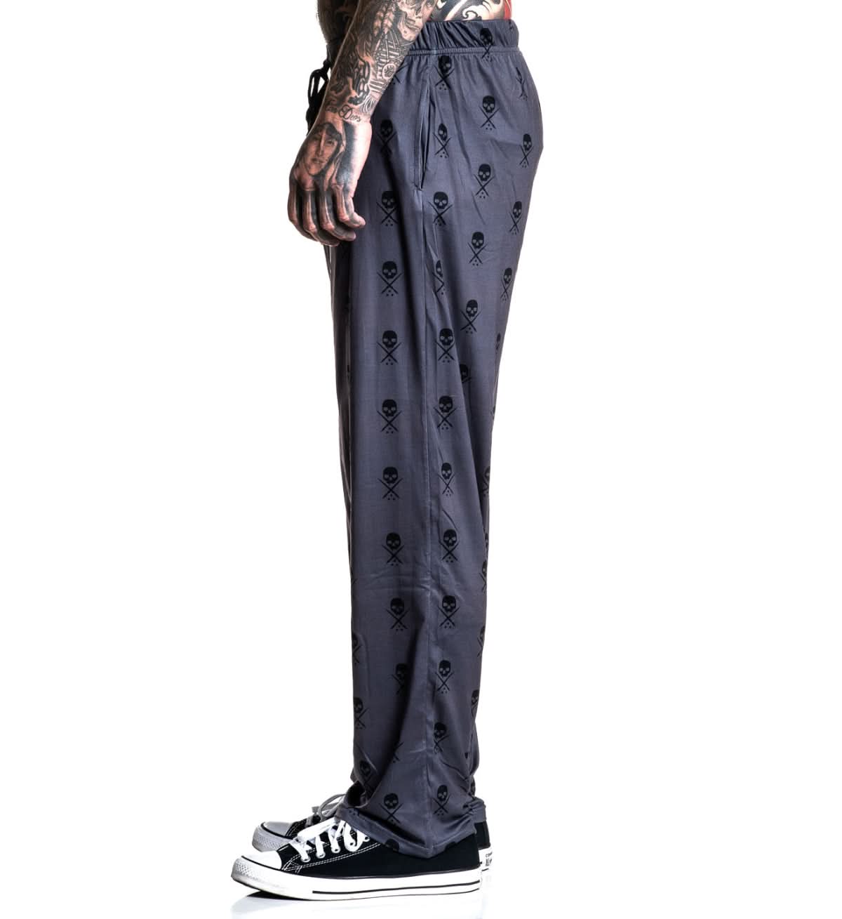 Dark gray pants with skull and crossbones pattern worn by a person on a white background