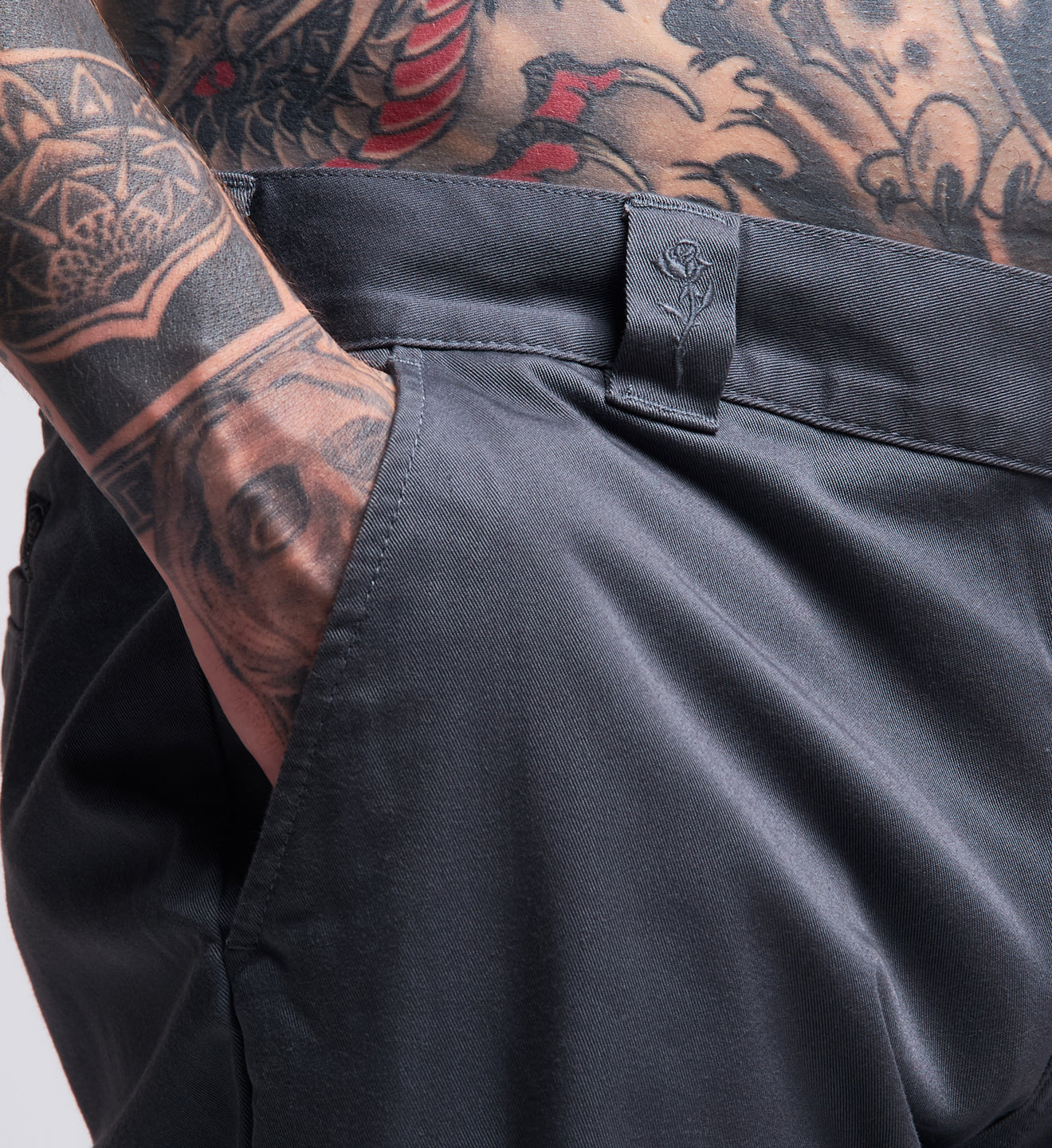 Person wearing black pants with a tattooed arm on a white background