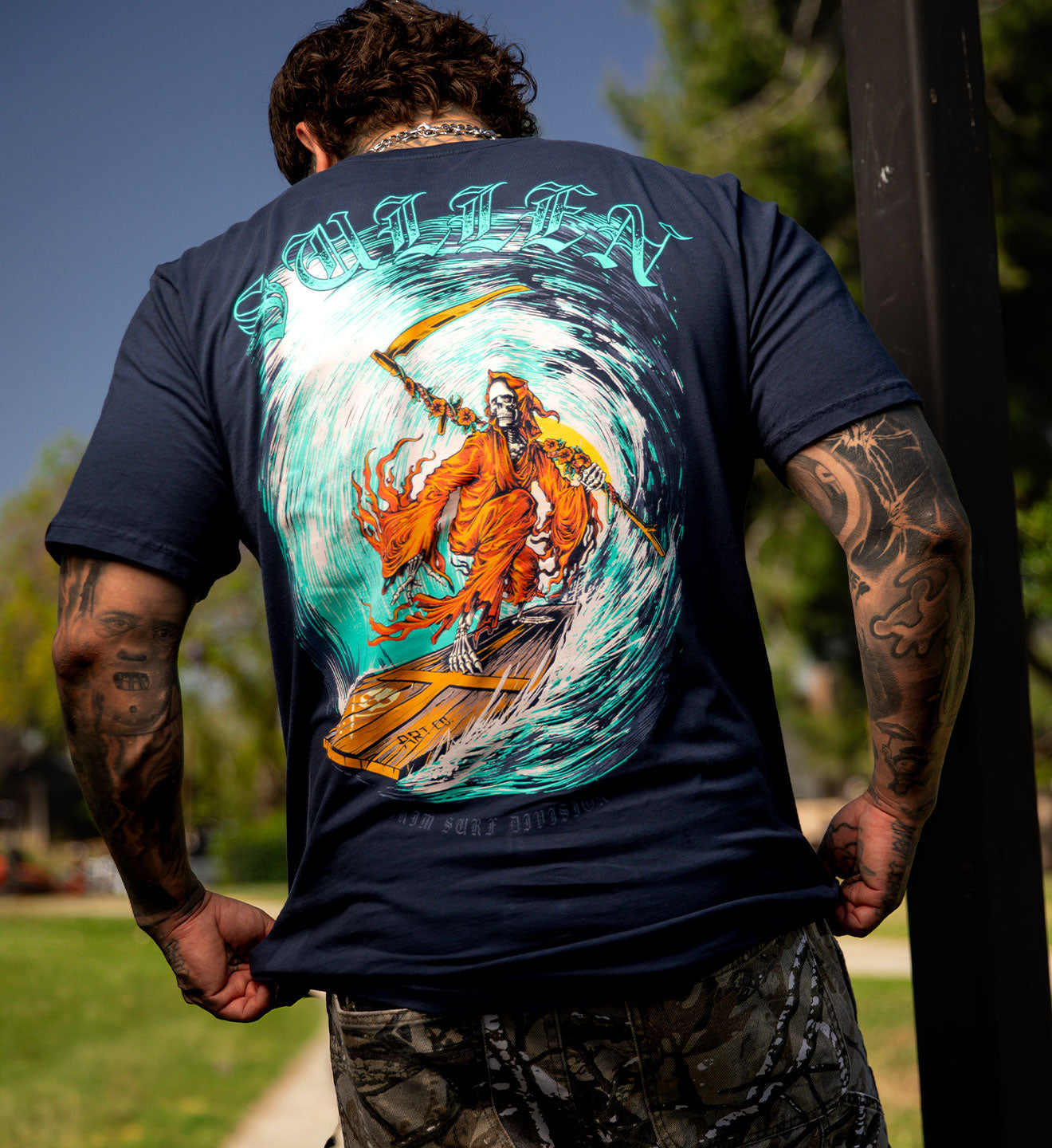 Person wearing a navy blue t-shirt with a colorful graphic design on the back, standing outdoors.