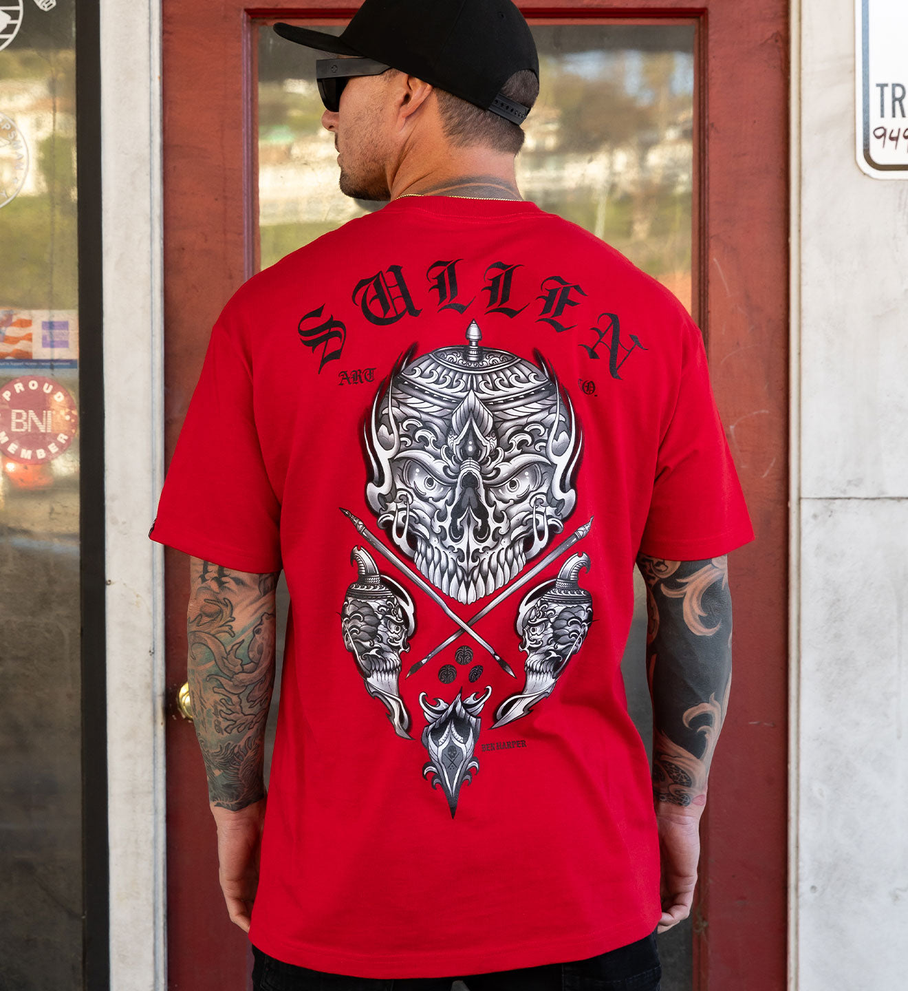 Person wearing a red 'Sullen' t-shirt with a skull design on the back, standing in front of a door.