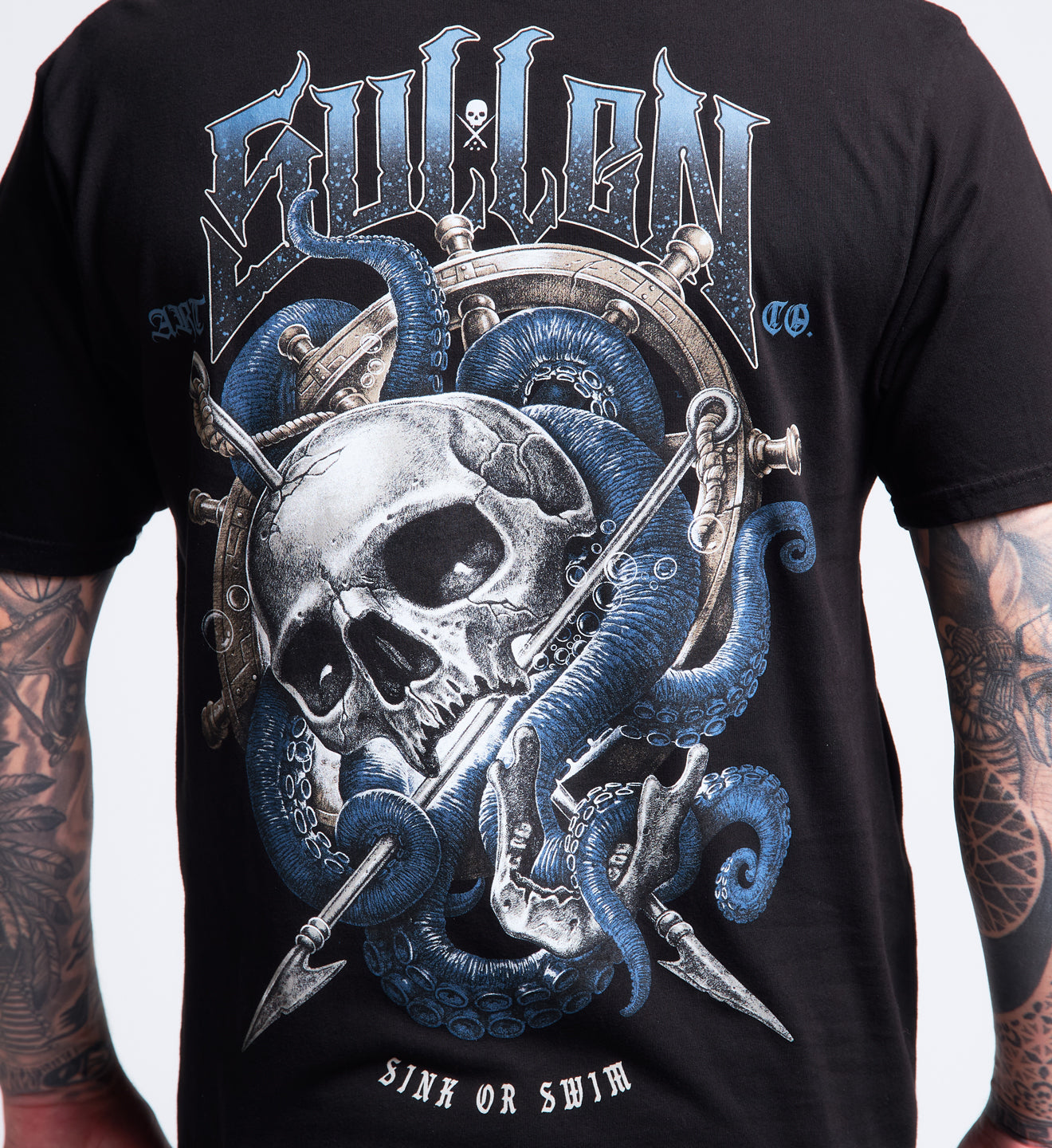 Black t-shirt with a skull and blue tentacles design on a person wearing tattoos.