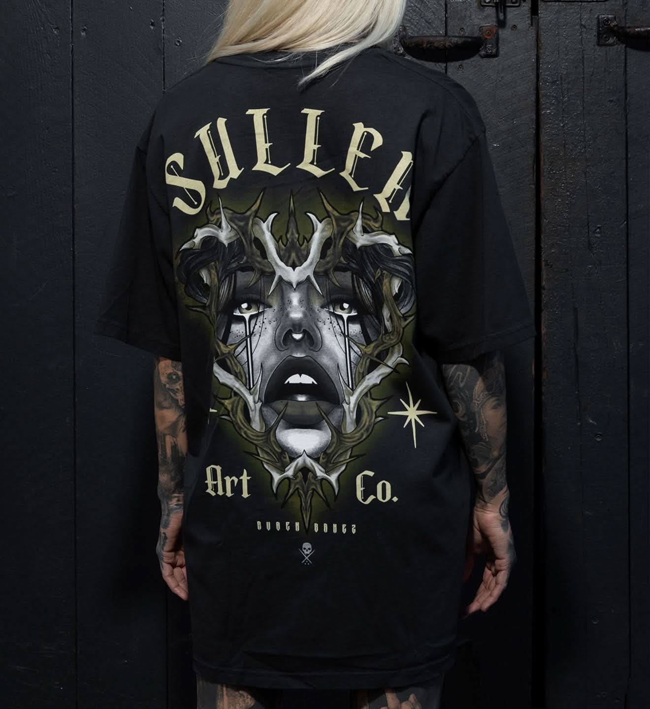 Person wearing a black t-shirt with a graphic design and text on the back against a dark background