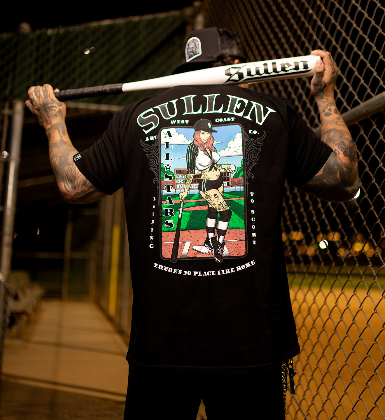 Person wearing a black t-shirt with 'Sullen' branding and graphic design, holding a baseball bat.