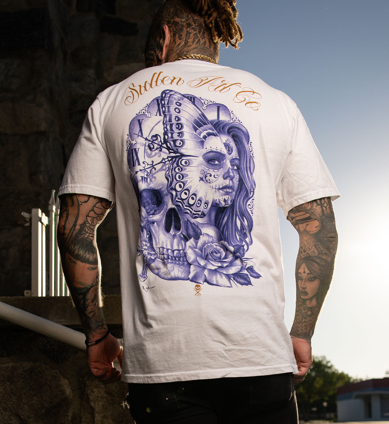Person wearing a white t-shirt with a graphic design of a skull and floral elements on the back.