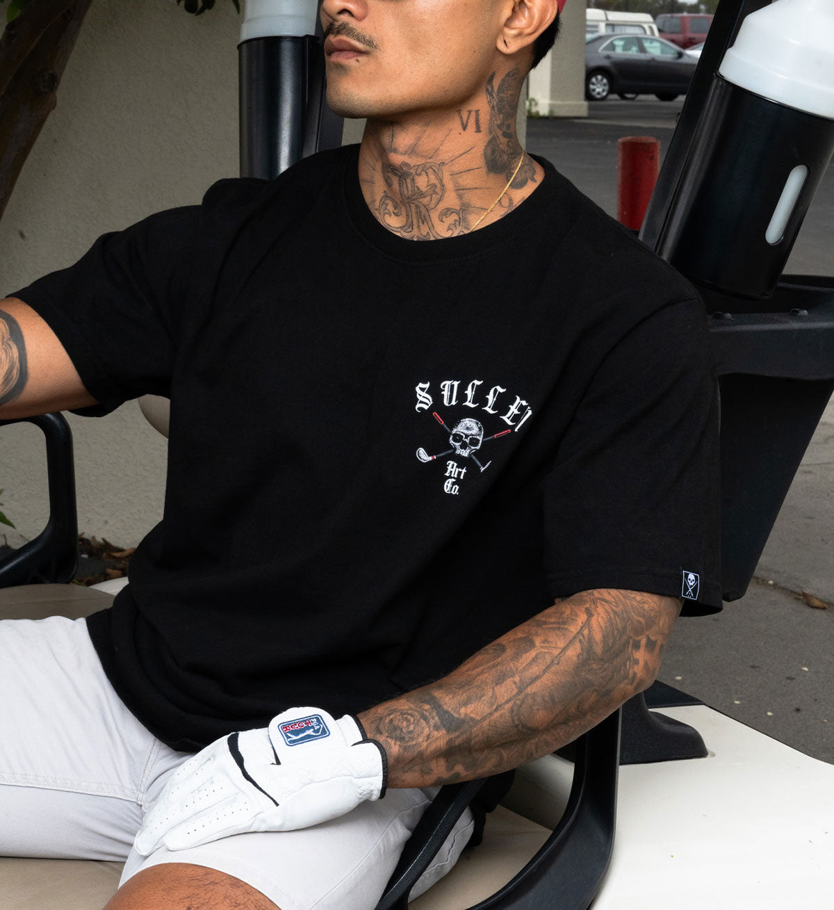 Man wearing a black t-shirt with a logo, sitting in a vehicle.