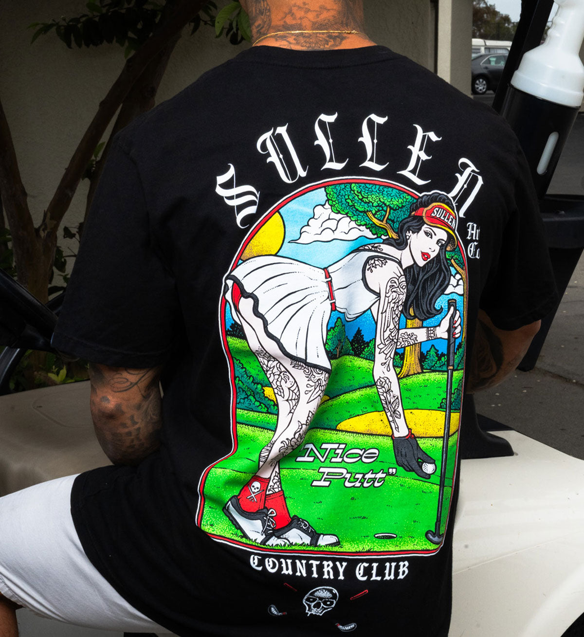 Person wearing a black t-shirt with a colorful graphic design on the back, featuring a golf-themed illustration.