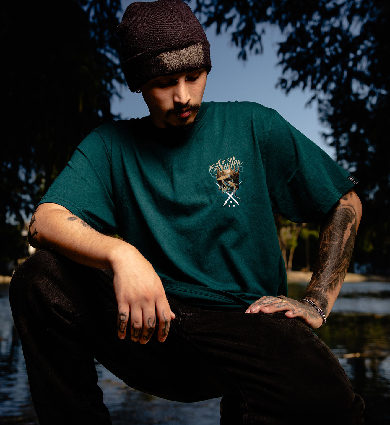 Person wearing a green t-shirt with a logo, sitting by a body of water.