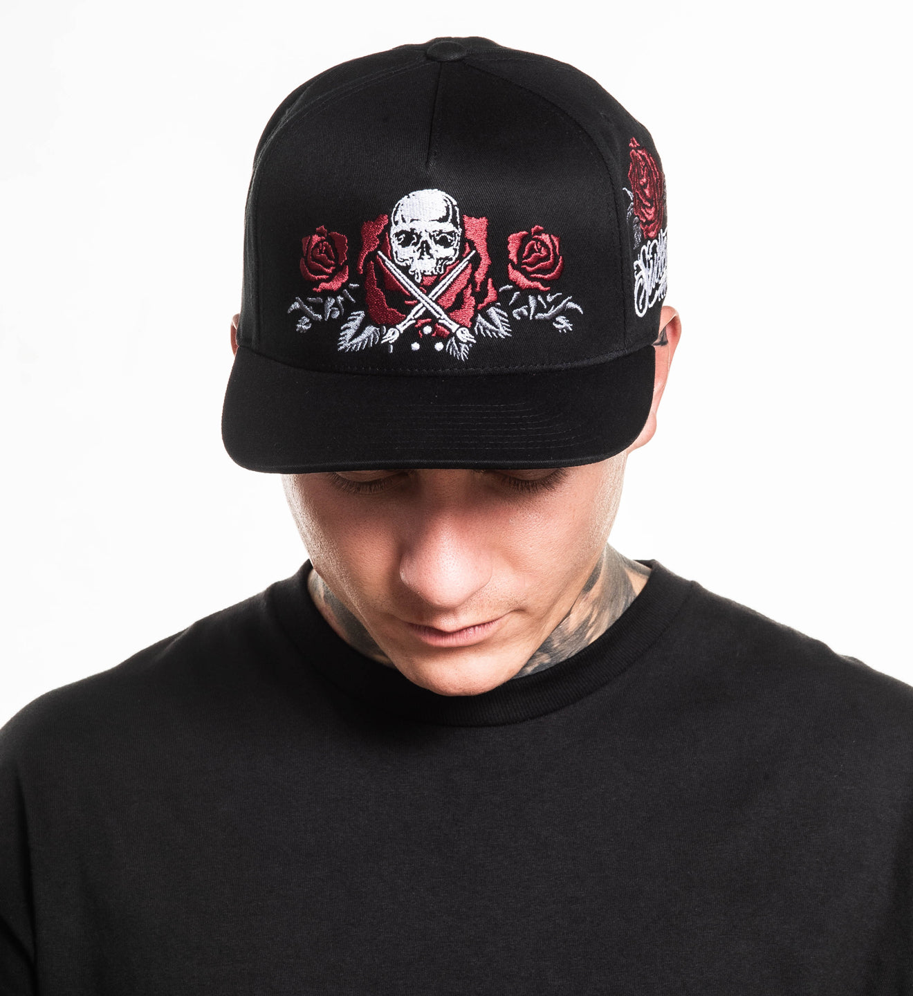 Person wearing a black cap with skull and roses design on a white background