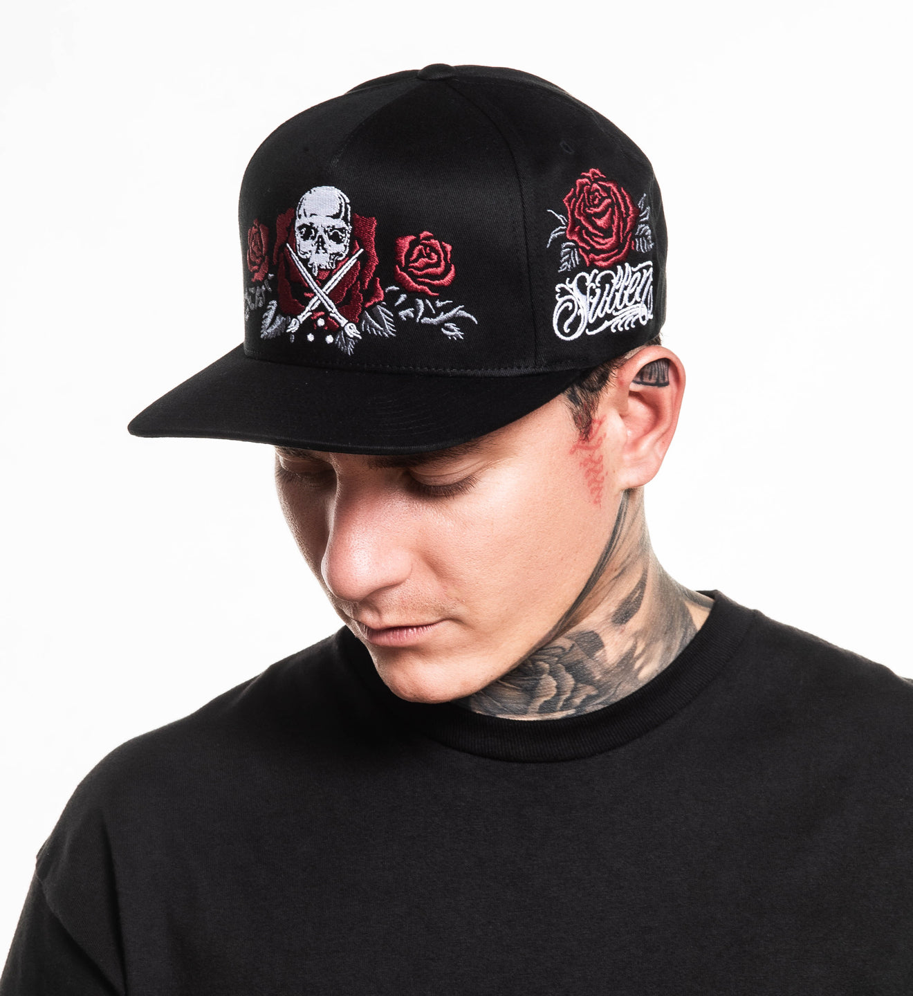 Person wearing a black cap with skull and roses design on a white background