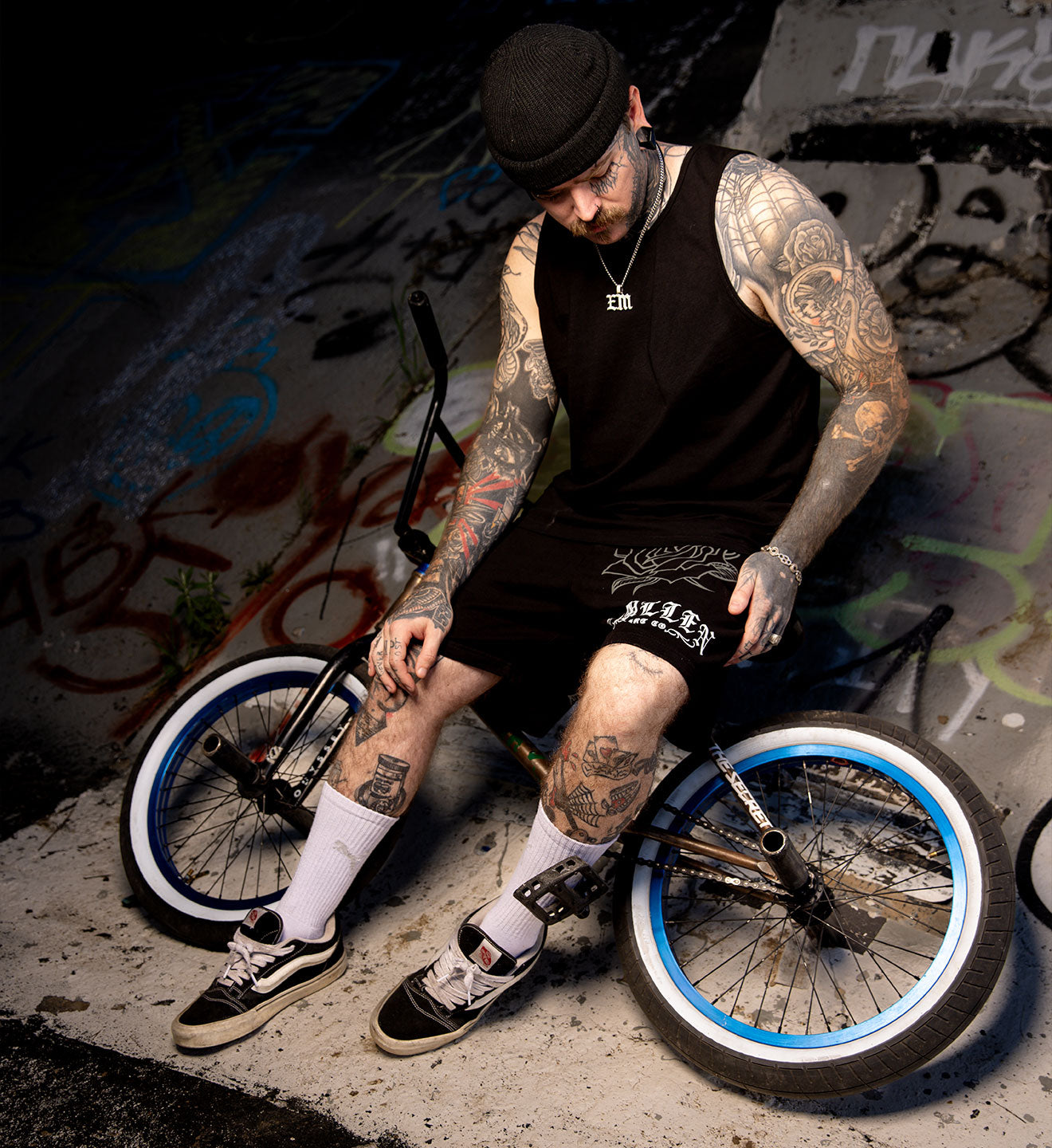 Man with tattoos sitting on a BMX bike against a graffiti-covered wall