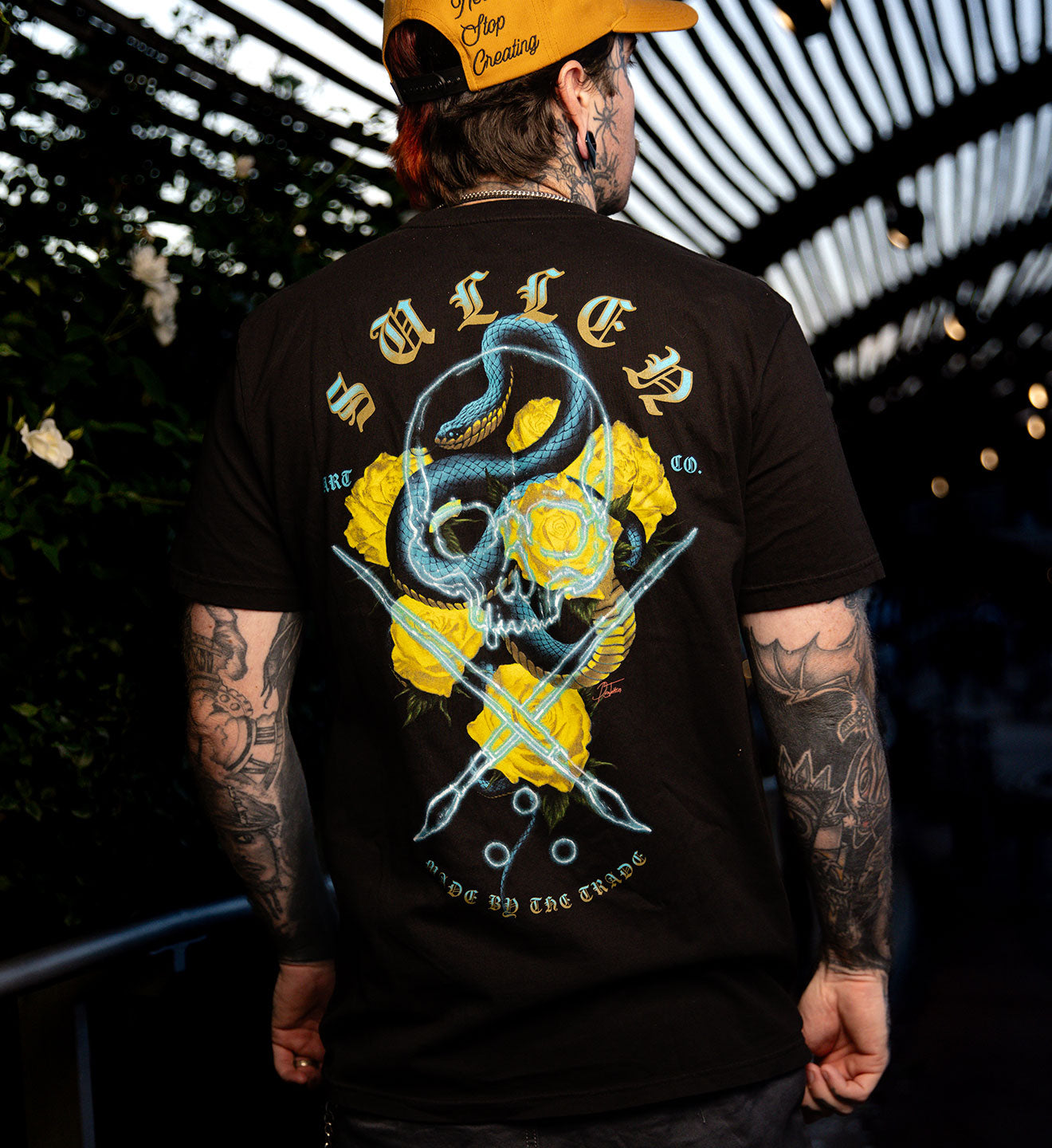 Person wearing a black t-shirt with a graphic design on the back, standing in an outdoor setting.