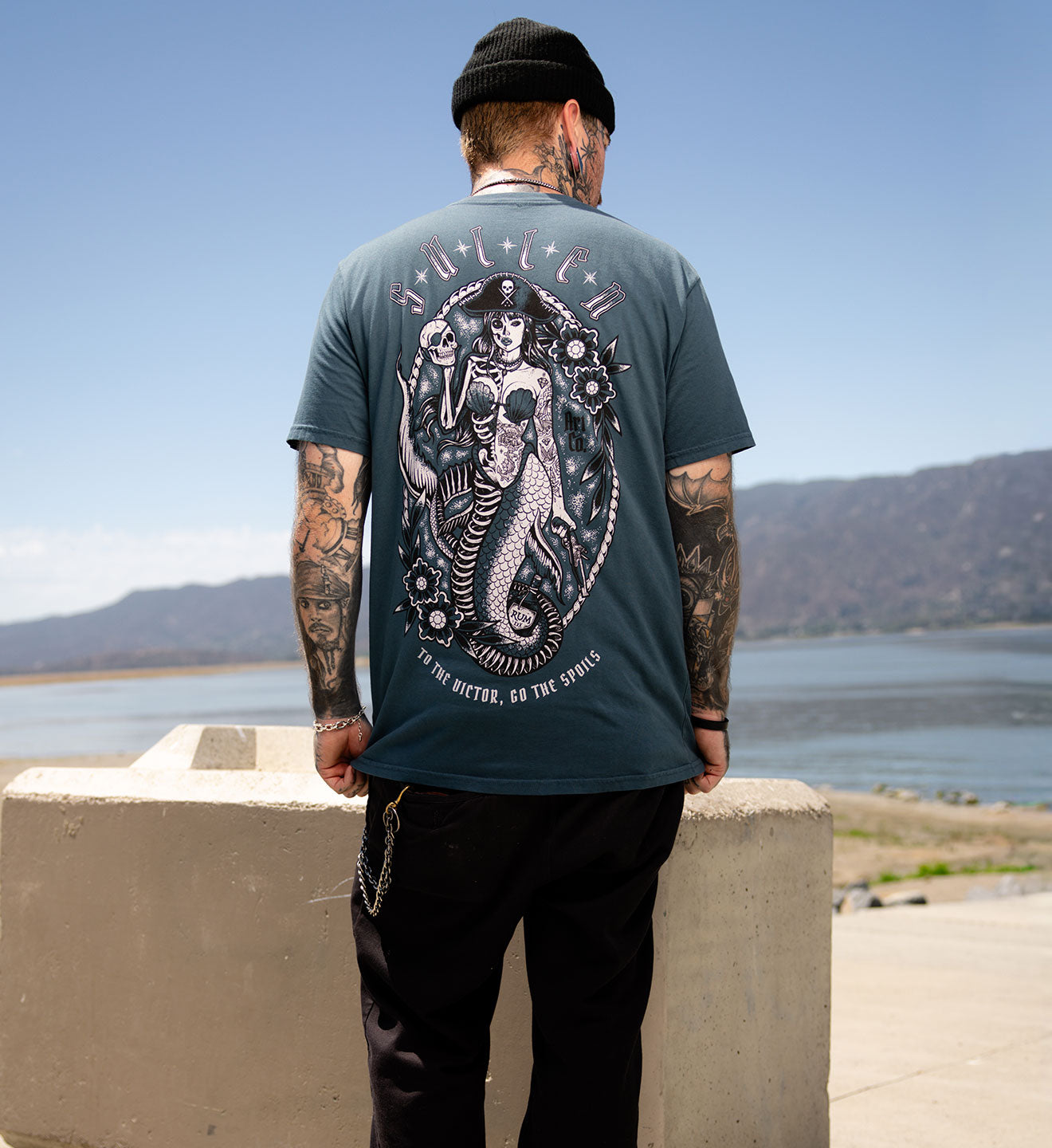 Person wearing a t-shirt with a graphic design outdoors by a body of water