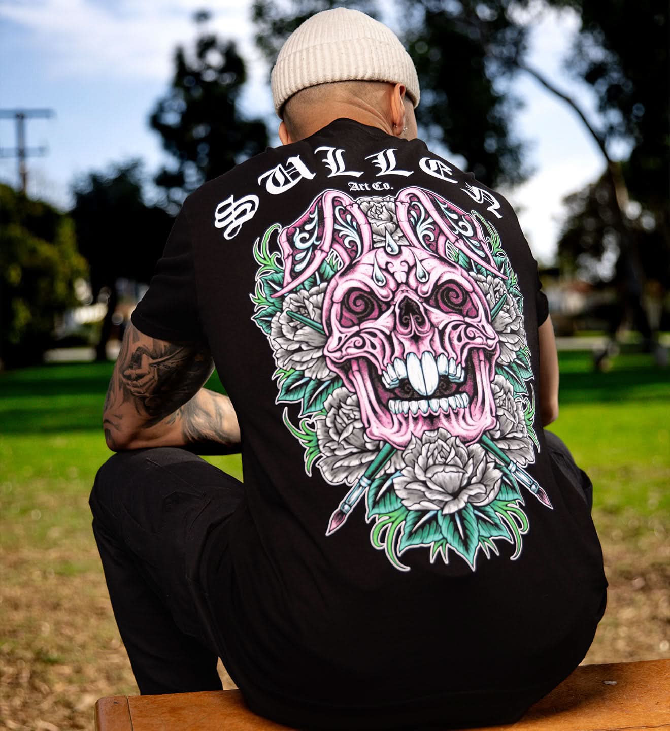 Person wearing a black sweatshirt with a colorful skull design on the back, sitting outdoors.