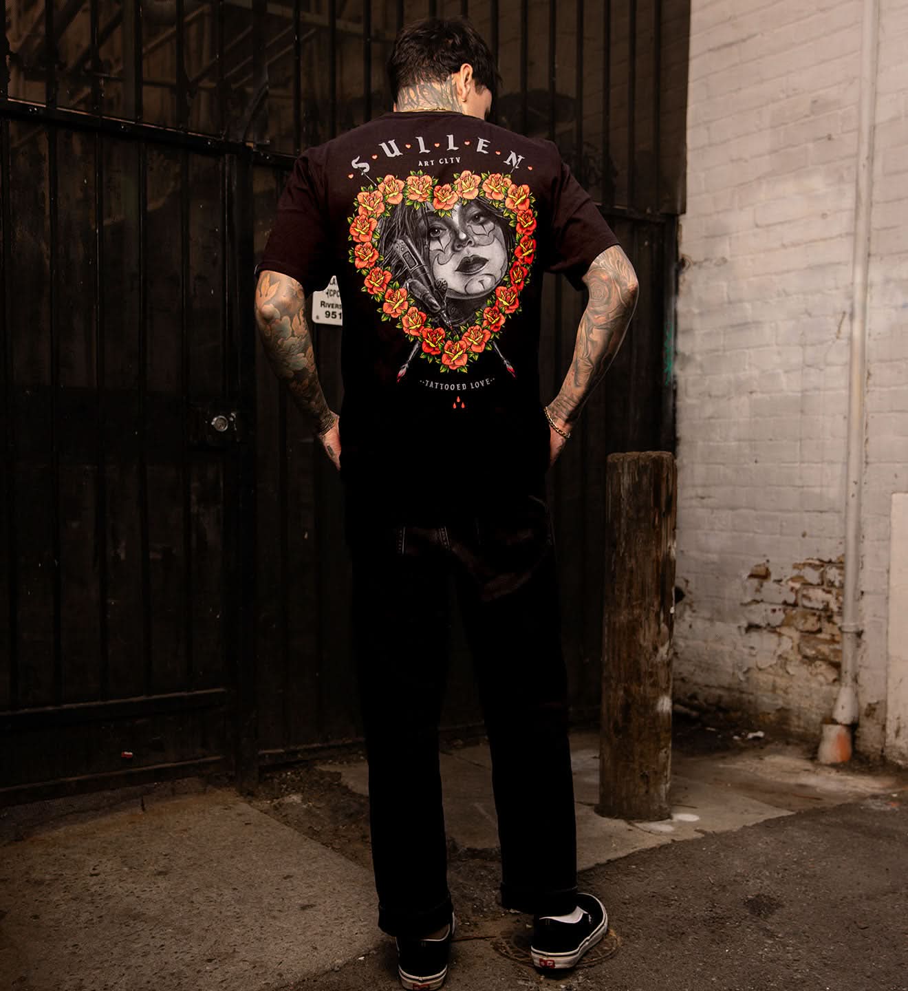 BLACK SULLEN T SHIRT WITH A SOFT GRAPHITE PORTRAIT OF A FEMALE TATTOOER FRAMED WITH TRADITIONAL COLORED ROSES IN THE SHAPE OF A HEART 