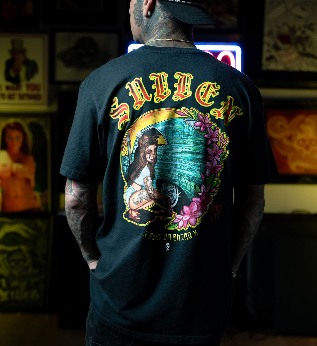 Person wearing a black t-shirt with a colorful graphic design on the back, featuring a woman holding a gun.