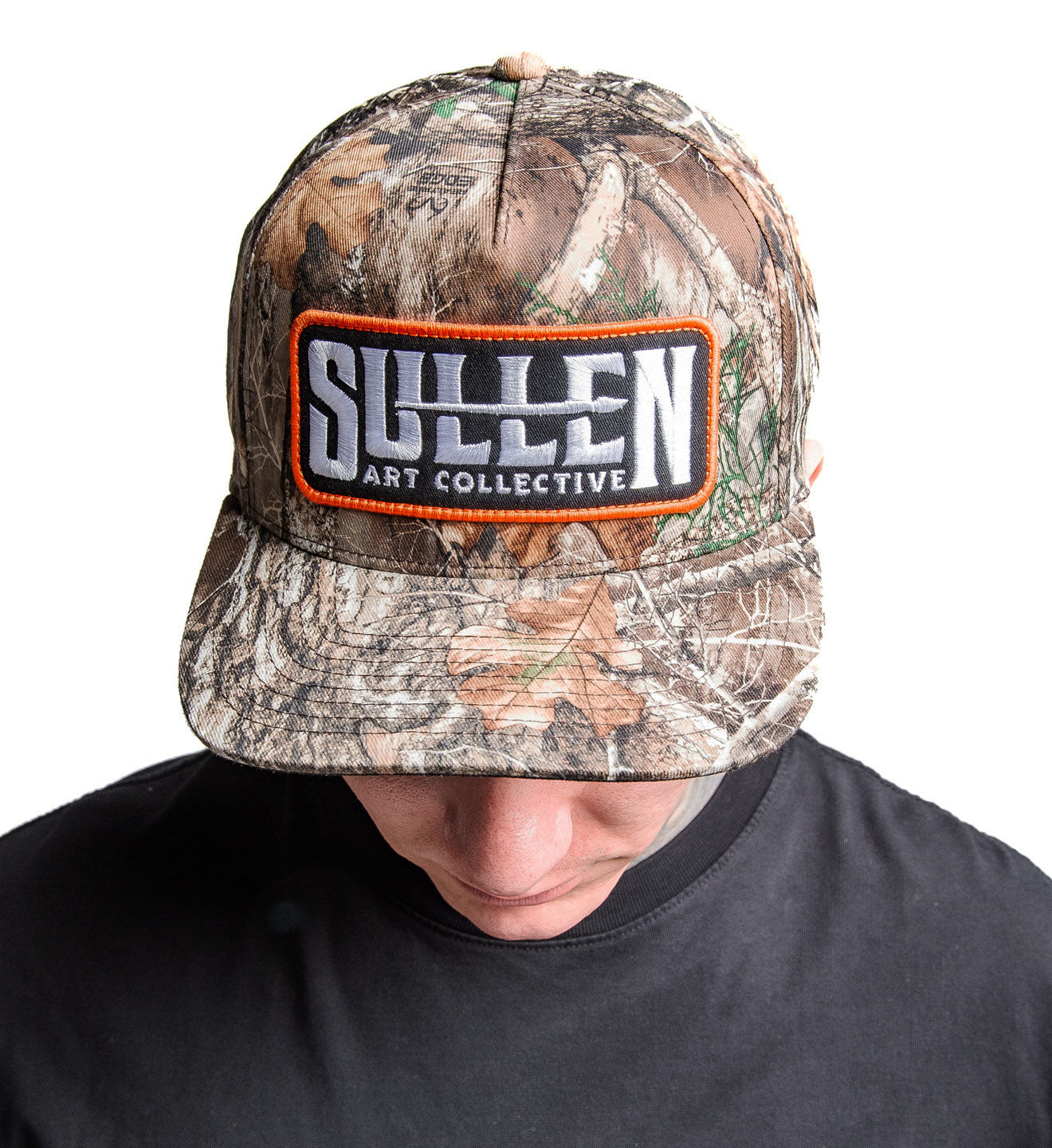 Camouflage cap with Sullen Art Collective logo worn by a person on a white background
