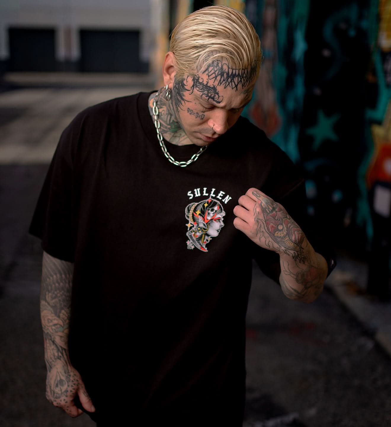 Person wearing a black Sullen t-shirt with tattoos visible on arms and neck.