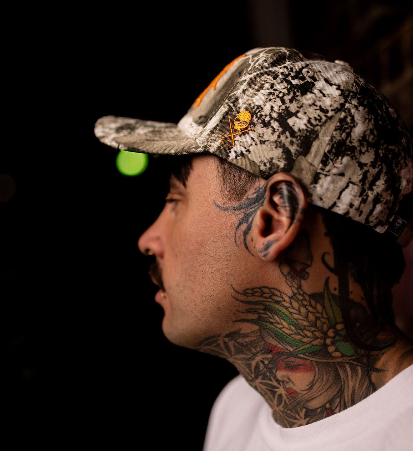Person wearing a camouflage cap with a logo, side view, dark background