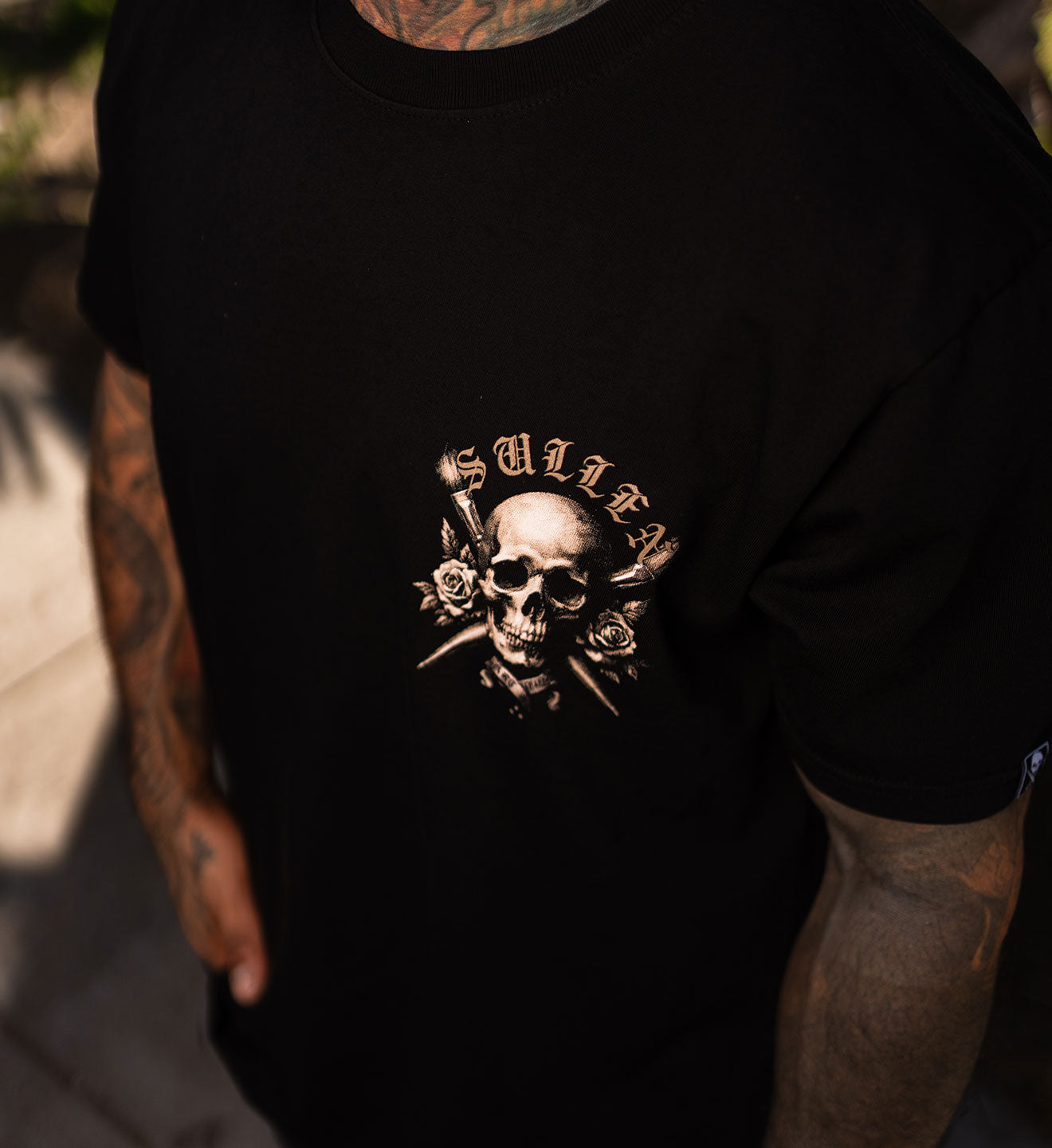 Black t-shirt with a skull and roses design on a person outdoors.
