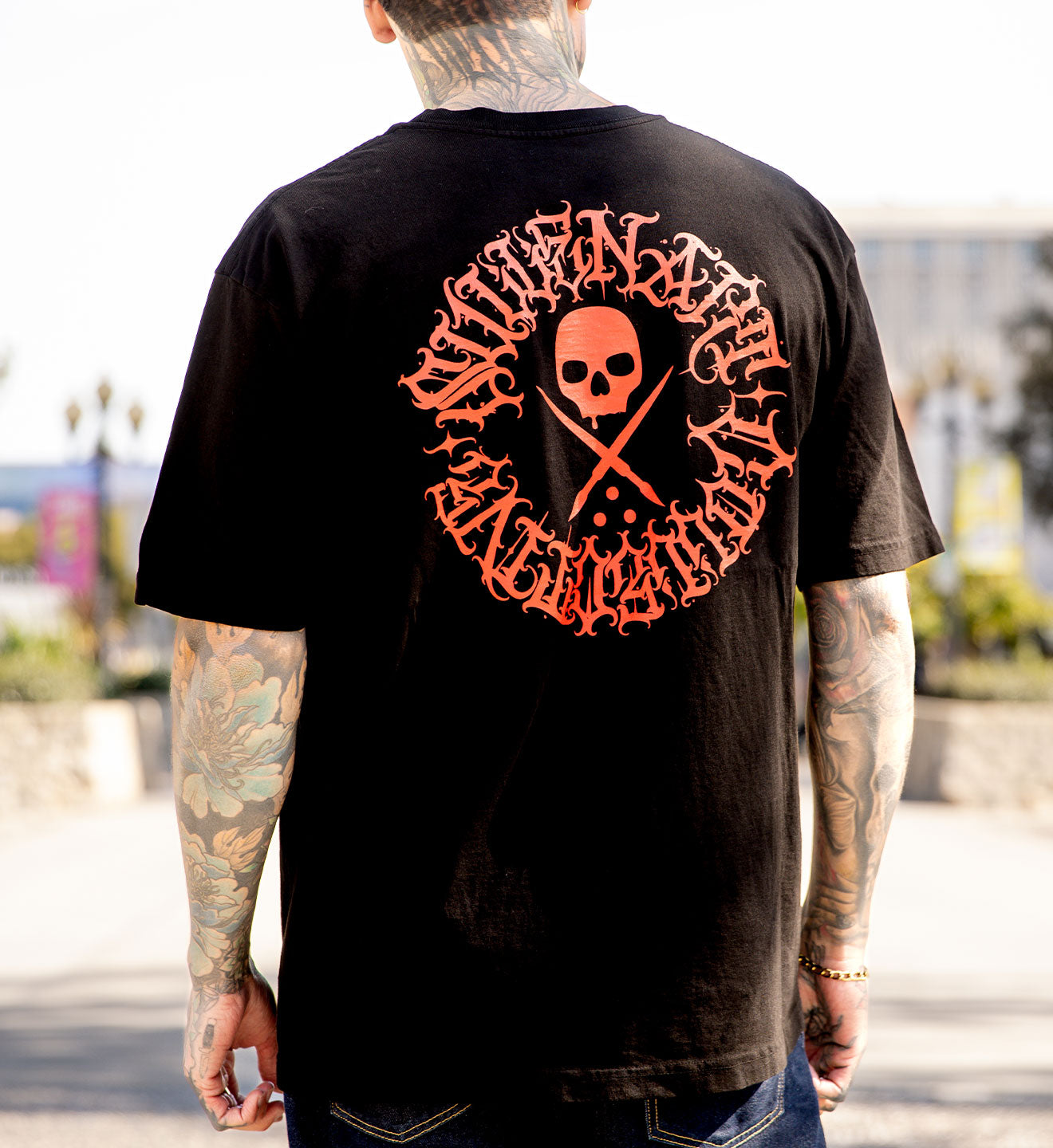 Person wearing a black t-shirt with a red and white graphic design on the back, standing outdoors.