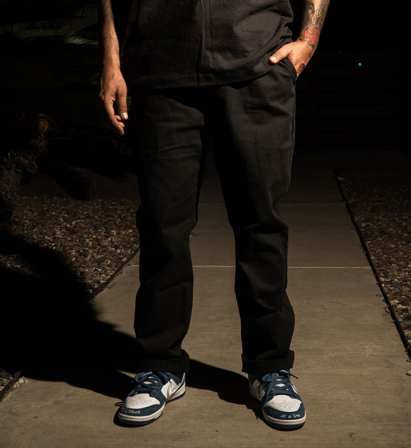 Person wearing black pants and blue sneakers standing on a dark pavement.