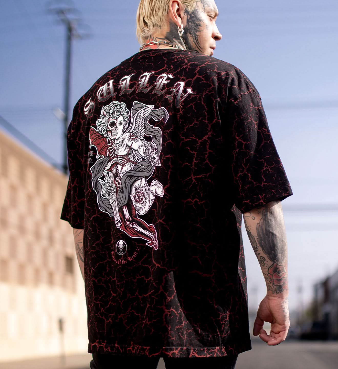 Person wearing a black graphic t-shirt with red accents and tattoos outdoors.