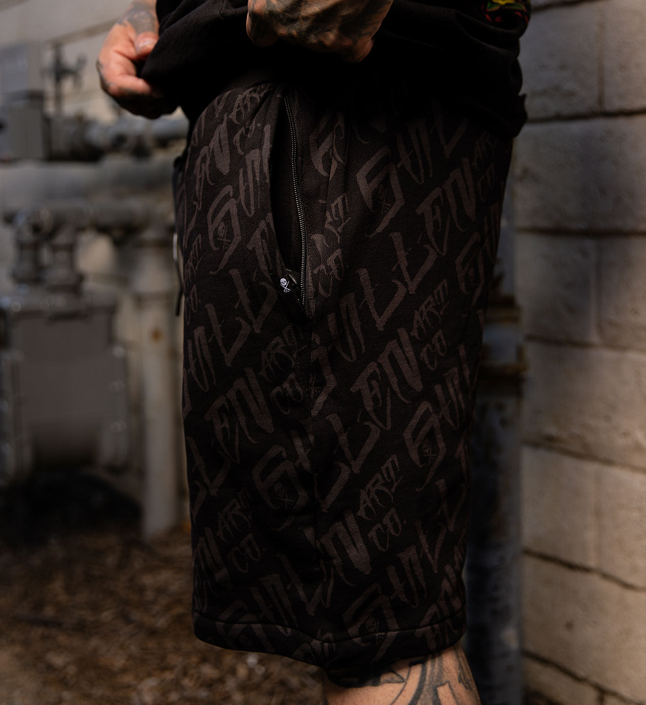 Person wearing black shorts with a pattern, standing against a stone wall.